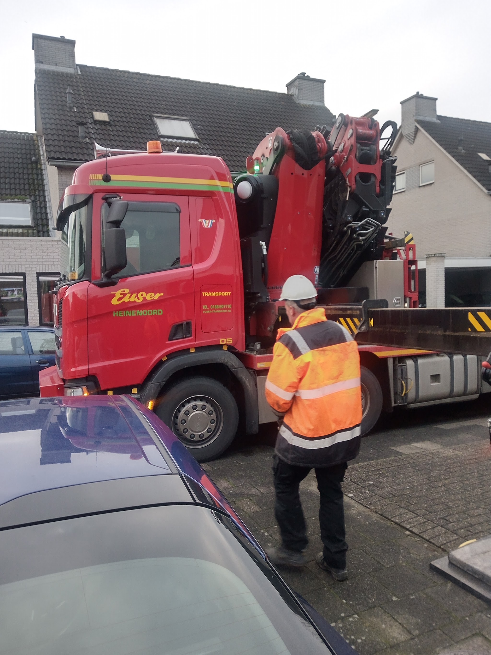 Kraanwagen in een woonstraat bij een klus, met iemand in oranje werkkleding en helm